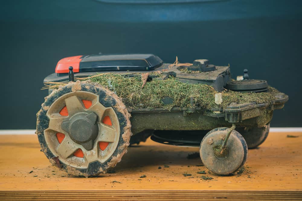 Dirty stripped robotic lawn mover on a wooden table ready to be serviced.