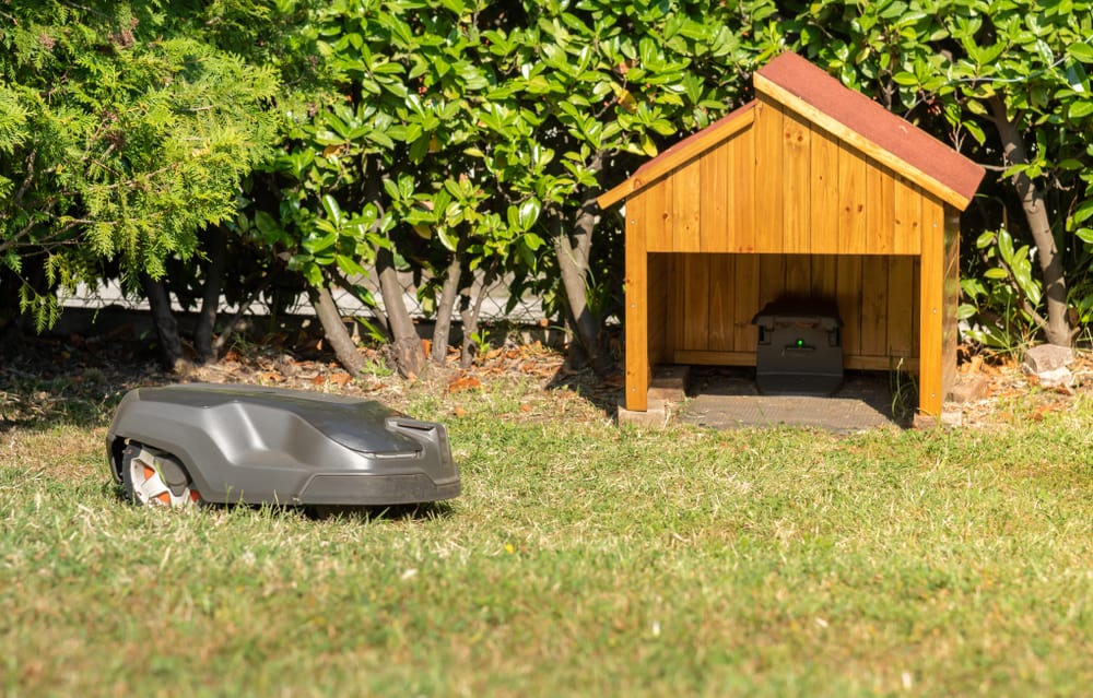 Robotic lawn mover on grass in garden. Returning to small wooden structure to recharge.