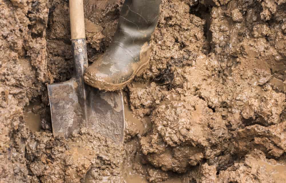 Man working with a shovel in clay soil.