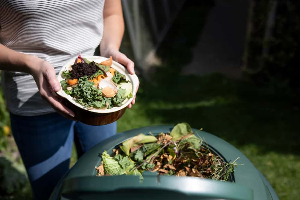 Woman emptying food waste into garden composter for organic composting.